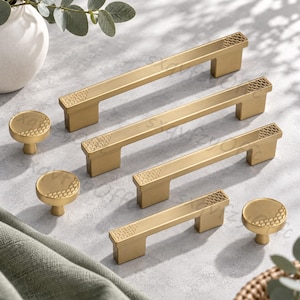 May include: A collection of brushed gold cabinet hardware including three rectangular bar pulls and three round knobs. Each piece features a textured fish scale pattern on the ends or edges, providing a consistent metallic finish and design.