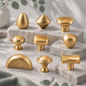 May include: A collection of nine gold-toned metal cabinet knobs and pulls in various geometric shapes, including round, square, semi-circular, and T-shaped designs, all featuring a smooth, matte finish and a consistent metallic gold colour.