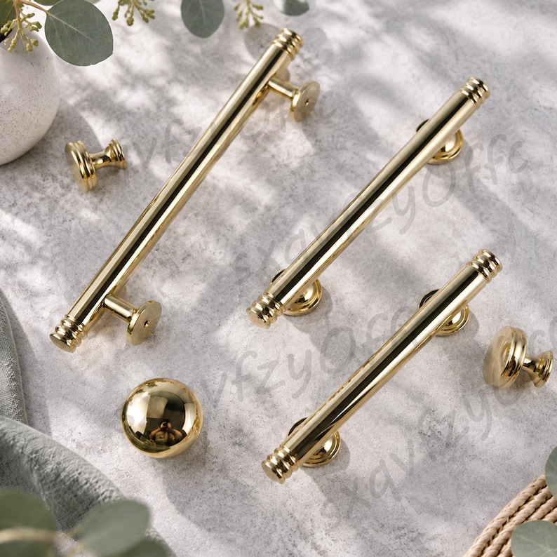 K&ouml;nnte beinhalten: Ein Set aus goldfarbenen Schrankbeschl&auml;gen, bestehend aus drei zylindrischen Stangengriffen mit gerippten Enden und zwei passenden runden Kn&ouml;pfen. Jedes Teil hat eine polierte metallische Oberfl&auml;che und kreisf&ouml;rmige Befestigungssockel.