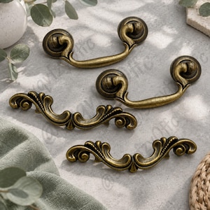 May include: Four antique brass-finished metal drawer pulls. Two pulls feature a simple curved handle with circular mounting ends, while the other two pulls display an ornate, scrolling leaf-like design with intricate detailing along the handle.