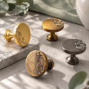 May include: Four round cabinet knobs in varying metallic finishes including brushed gold, antique brass, and dark gunmetal. Each knob features a raised, swirling wave-like pattern on one side of the circular face and a central mounting post.