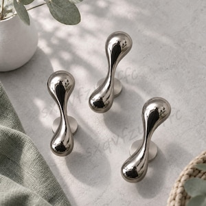 May include: Three silver-toned metal wall hooks with a smooth, reflective, teardrop-shaped design. Each hook features a rounded, bulbous top and a narrower base that connects to a circular mounting plate, creating a sleek, polished appearance.