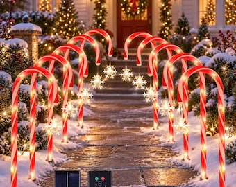 May include: A set of red and white striped candy cane pathway lights with hanging illuminated snowflake ornaments. The lights are powered by a black solar panel and a control box with buttons, designed for outdoor holiday decoration.