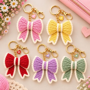 Puede incluir: Cinco llaveros de lazos tejidos a ganchillo en rosa, amarillo, rojo, morado y verde salvia. Cada lazo incluye un cierre de mosquetón de metal dorado, una cadena corta y un pequeño dije en forma de corazón con un borde blanco.