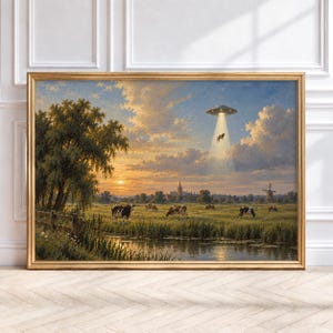 May include: A framed landscape painting depicting a rural pasture at sunset with grazing black and white cows, a distant windmill, and a metallic flying saucer hovering in the sky, beaming a bright light down to lift a cow into the air.