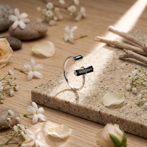 May include: A silver open-style ring featuring two black rectangular stones. One stone is a small square shape, and the other is a larger elongated baguette shape. The ring has a thin, polished metal band that remains open at the front.