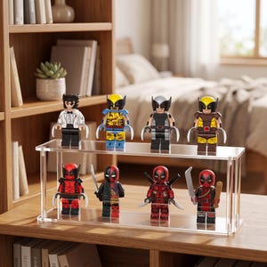 Könnte beinhalten: Ein zweistufiger Präsentationsständer aus klarem Acryl mit acht Miniatur-Actionfiguren. Die obere Reihe zeigt vier Figuren mit Klauen-Zubehör, während die untere Reihe vier Figuren enthält, darunter zwei mit Schwertern und eine mit einem Holzknüppel.