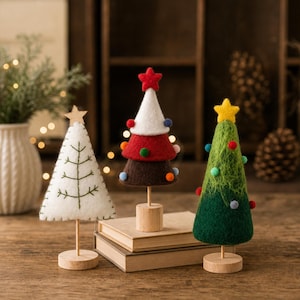 May include: Three cone-shaped decorative trees on wooden stands. The left tree is white felt with green stitched branches and a wooden star. The center tree has white, red, and brown felt layers with small colorful pom-poms and a red star. The right tree is green fiber with small colorful pom-poms and a yellow star.