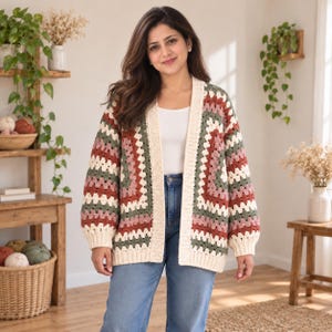 Op de afbeelding: Een gehaakt vest met lange mouwen en een granny square patroon in afwisselende strepen van crème, saliegroen en oudroze. Het vest is aan de voorzijde open en heeft een effen crème geribbelde boord langs de halslijn en de mouwboorden.