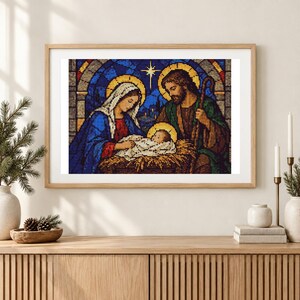 May include: A framed cross-stitch artwork depicting a nativity scene with Mary, Joseph, and the infant Jesus in a manger. The figures are rendered in a stained-glass style with vibrant blue, green, and gold tones, set against a dark background.