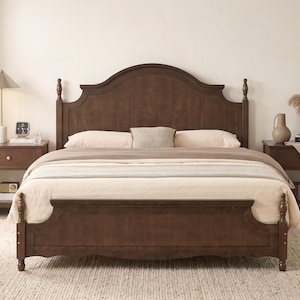 May include: A dark brown wooden bed frame with a tall, arched headboard and a matching footboard featuring turned posts. The bed is dressed with a light beige comforter, two matching pillows, and a small rectangular accent pillow in the center.