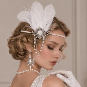 May include: A white feather headpiece featuring a silver-toned floral centerpiece with dangling pearl chains, paired with matching drop earrings and a pearl necklace. The headpiece is worn across the forehead with a delicate pearl-beaded band.