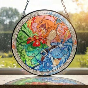 May include: A circular stained glass suncatcher featuring three creatures: an orange fire-breathing dragon, a green plant-based creature with a red flower, and a blue turtle-like creature with cannons, all framed by a decorative border and hanging chain.