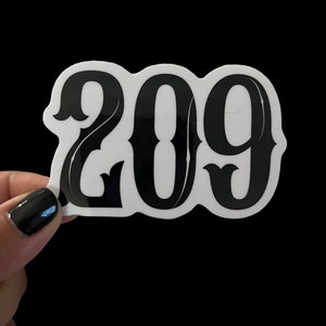 May include: A white sticker with the black number "209" in a bold, decorative font. The sticker is held against a black background. The number has a vintage, western-style design.