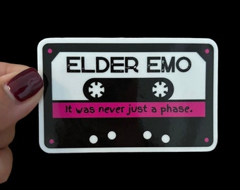 Può includere: Un adesivo bianco a forma di cassetta con dettagli neri e rosa. L'adesivo presenta il testo "ELDER EMO" e la frase "It was never just a phase."