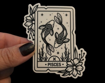 May include: Black and white sticker featuring a stylized illustration of two fish swimming in a circle, with a floral border and the text "PISCES" and the astrological symbol for Pisces.