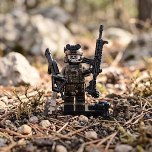 May include: A tactical soldier minifigure wearing a camouflage uniform, a helmet with night vision goggles, and a skull-patterned face mask. The figure holds a black rifle and a shovel, with additional gear including binoculars and a small canister.