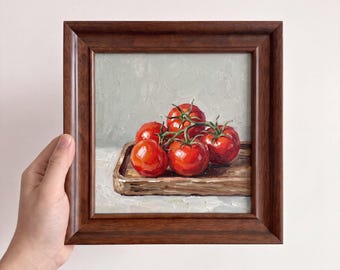 Puede incluir: Una pintura al óleo en un marco de madera marrón oscuro que representa un racimo de cinco tomates de color rojo brillante con tallos verdes sobre una pequeña bandeja de madera. El fondo es una superficie gris claro texturizada.