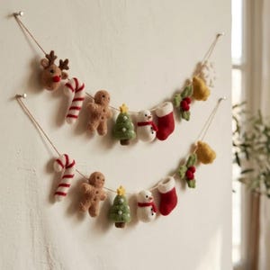 May include: A two-tiered Christmas garland featuring felted ornaments strung on twine. The ornaments include a reindeer, candy canes, gingerbread people, Christmas trees with yellow stars, snowmen, red stockings, and holly sprigs with berries.