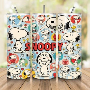 May include: A cylindrical stainless steel tumbler featuring a repeating pattern of Snoopy in various poses against a light blue checkered background. The design includes red hearts, yellow stars, and the word SNOOPY in bold red letters. Includes a metal straw.