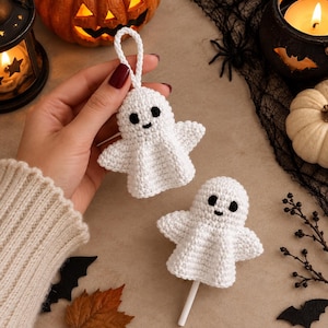 Puede incluir: Dos adornos de fantasma tejidos en crochet blanco con ojos y bocas bordados en negro. Un fantasma tiene un lazo de hilo blanco para colgar, mientras que el otro está unido a un palo blanco. Ambos tienen cabezas redondas y cuerpos acampanados.