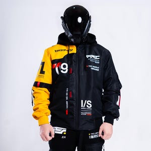 Peut inclure: Une veste à capuche présentant un design bicolore avec une manche droite jaune vif et un côté gauche noir. Le vêtement affiche des textes graphiques blancs et rouges, incluant les caractères 09, I/S et divers marquages techniques.