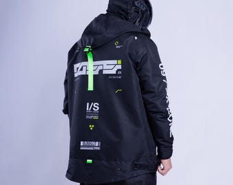May include: A black hooded jacket featuring white and neon green graphic prints, including text and geometric patterns. The jacket has a bright neon green strap on the hood, long sleeves with white text, and a black hood covering the head.