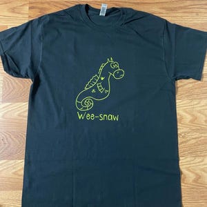 Pode incluir: Camiseta preta com um contorno verde de um cavalo-marinho de desenho animado e o texto "Wee-snaw".