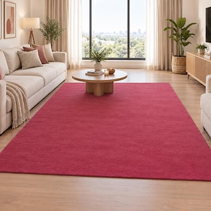 Puede incluir: Una alfombra rectangular grande de color rosa magenta intenso y sólido. La alfombra presenta una textura uniforme de pelo corto y está colocada centralmente sobre un suelo de madera clara, extendiéndose desde el frente hacia los muebles.