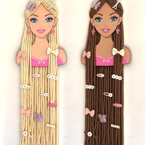 May include: Two wall-mounted hair clip organizers shaped like doll busts, one with long blonde yarn hair and one with long brown yarn hair. Both feature pink tops, heart-shaped earrings, and various decorative hair clips including bows, flowers, and butterflies.