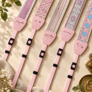 May include: Five camera straps with woven fabric patterns in shades of pink, purple, and blue. Each strap features a light pink faux leather end piece personalized with names or initials including Samantha, J|K, Good Photos, OLIVIA, and C/D.