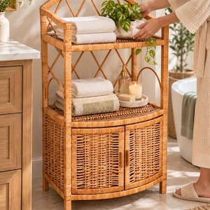 May include: A light brown wicker bathroom storage unit featuring an arched top, an open middle shelf, and a lower cabinet with two doors. The unit is constructed with woven rattan material and includes a lattice-style back panel design.