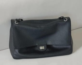 May include: A black leather shoulder bag with a pebbled texture, featuring a rectangular flap, a silver-toned metal turn-lock closure, and silver-toned grommets where the shoulder straps attach to the top of the bag body.