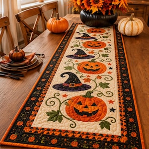 May include: A rectangular quilted table runner featuring a cream-coloured centre panel with a repeating pattern of orange jack-o'-lanterns, purple witch hats, green leaves, and small orange and black stars, bordered by a black and orange fabric trim.