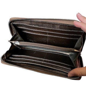 May include: Open, brown leather wallet with a silver zipper. The interior features multiple card slots and a zippered coin compartment. The brand name "CHANEL" is visible inside the wallet.