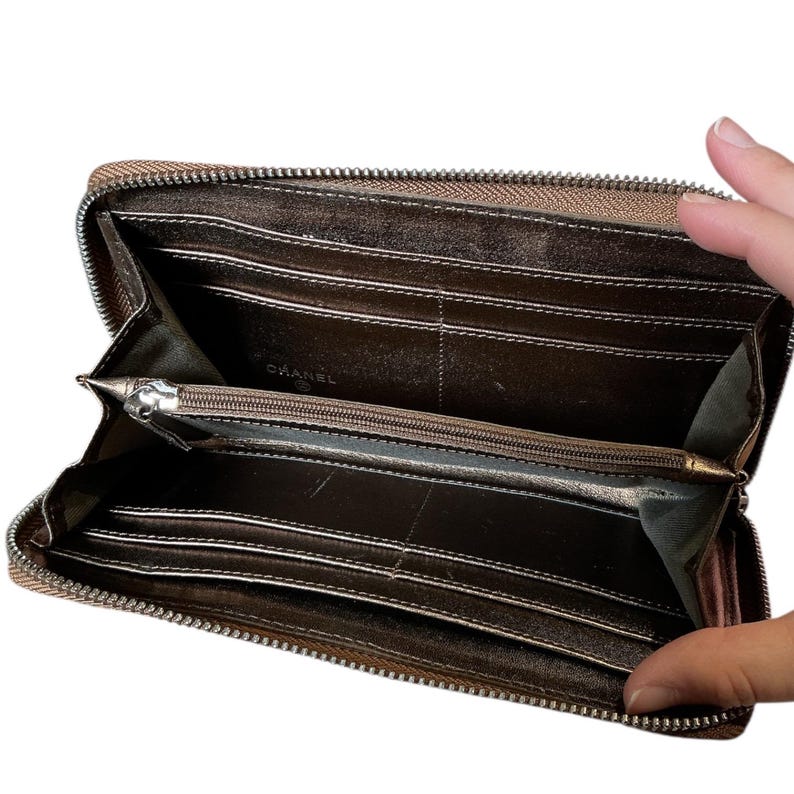 May include: Open, brown leather wallet with a silver zipper. The interior features multiple card slots and a zippered coin compartment. The brand name "CHANEL" is visible inside the wallet.
