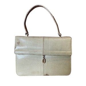 Könnte beinhalten: Hellbeige Handtasche mit strukturierter, reptilienartiger Musterung. Die Tasche hat einen Klappverschluss mit goldfarbener Schnalle und einen einzelnen Henkel.