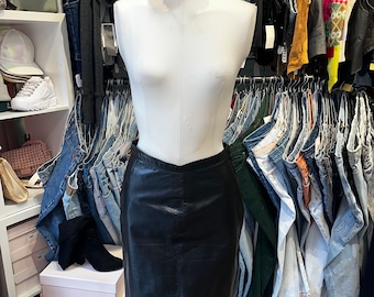 May include: A black leather mini skirt on a white mannequin. The skirt is a classic style with a straight cut and a simple design.