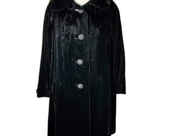 May include: A long, black velvet coat with a wide collar and three decorative buttons. The coat is buttoned up and appears to be vintage. The fabric has a soft, luxurious sheen.
