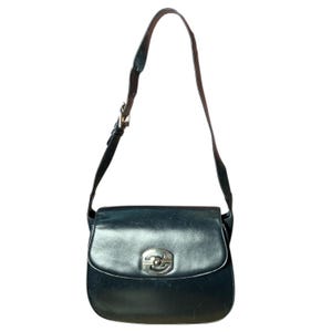 May include: Black leather shoulder bag with a silver clasp. The bag has a curved shape with a flap closure and a long, adjustable strap. White stitching and a vintage appearance are visible.