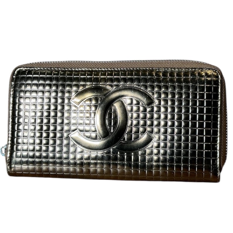 May include: Metallic silver wallet with a grid pattern and a prominent interlocking double-C logo. The wallet has a zipper closure and a textured surface, suggesting a high-end design. The overall aesthetic is sleek and modern.
