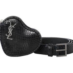 Könnte beinhalten: Ein schwarzer Gürtel und eine herzförmige Münztasche mit Schlangenleder-Textur. Die Tasche hat einen silbernen Reißverschluss und ein silbernes Logo. Der Gürtel hat eine silberne Schnalle.