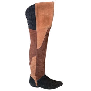 May include: A knee-high boot with a flat sole. The boot is made of suede in a patchwork design of black, brown, and tan. The back of the boot has a lace-up detail. The boot is designed to be worn over the knee.
