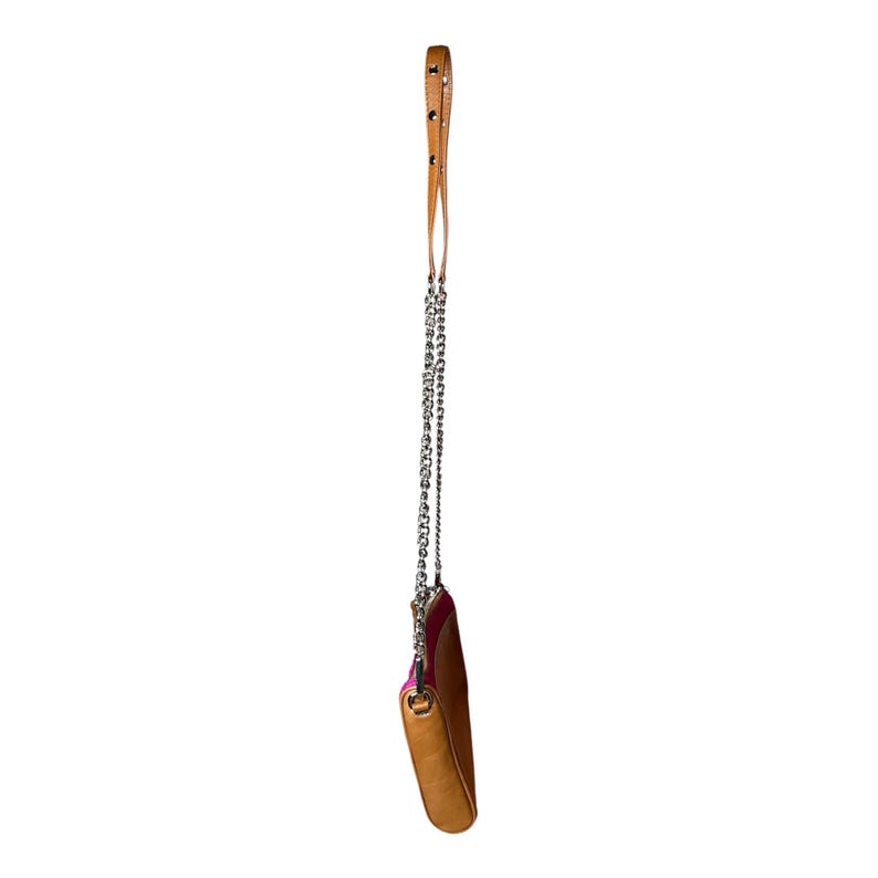 Puede incluir: Un peque&ntilde;o bolso bandolera de cuero marr&oacute;n claro con una correa de cadena plateada y un asa de cuero marr&oacute;n claro a juego. El bolso tiene un interior rosa y est&aacute; suspendido sobre un fondo blanco.
