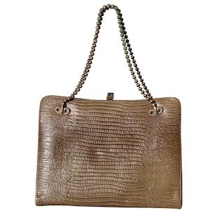 May include: A rectangular, tan handbag with a textured, reptile-like pattern. The bag features a beaded chain handle and a clasp closure. The hardware is gold-toned, and the bag has a vintage aesthetic.