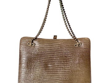 May include: A rectangular, tan handbag with a textured, reptile-like pattern. The bag features a beaded chain handle and a clasp closure. The hardware is gold-toned, and the bag has a vintage aesthetic.