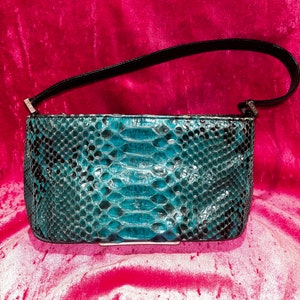 Puede incluir: Un bolso de mano de piel de serpiente turquesa con una correa de hombro negra. El bolso tiene un cierre plateado.