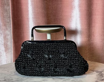 May include: A black vintage handbag with a woven texture and a glossy frame. The bag features a curved handle and silver-toned hardware. The bag is approximately 25 cm wide.