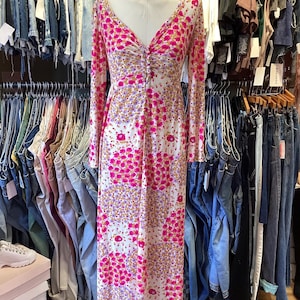 May include: A white maxi dress with a pink floral pattern. The dress has a V-neckline and long sleeves. It is displayed on a mannequin in a clothing store.