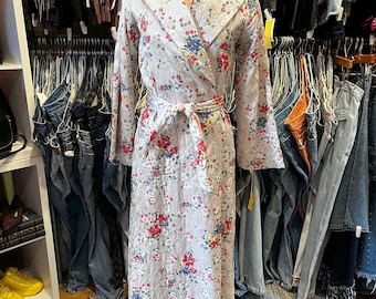 May include: A white quilted robe with a floral print featuring pink, red, and blue flowers. The robe has a shawl collar and a tie belt.